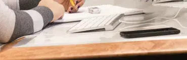 person holding a writing implement using a notepad, sitting in front of a computer