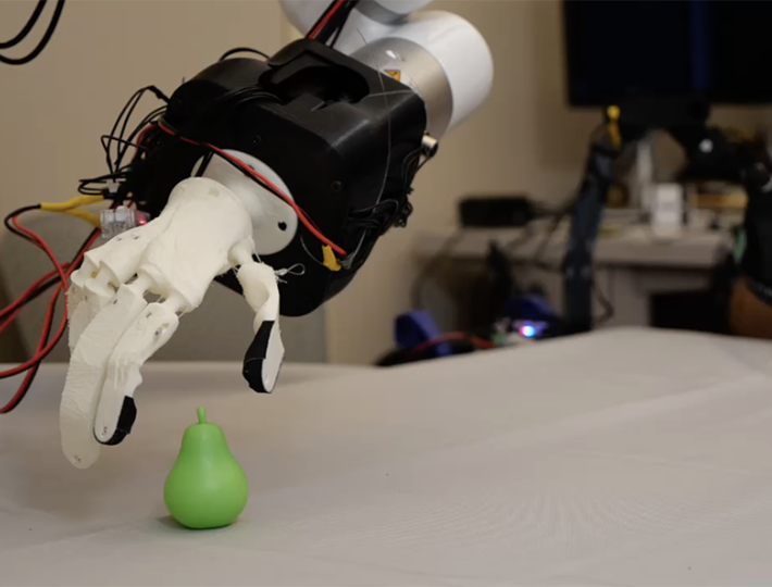 A robotic hand made with a white plastic material reaches out to grasp a green toy pear.