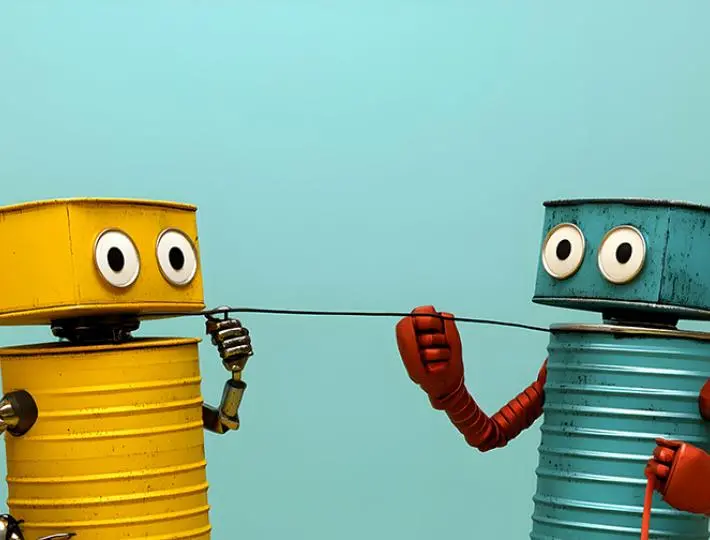 A yellow robot made from tin cans talks to a blue robot, also made from tin cans, using a string.