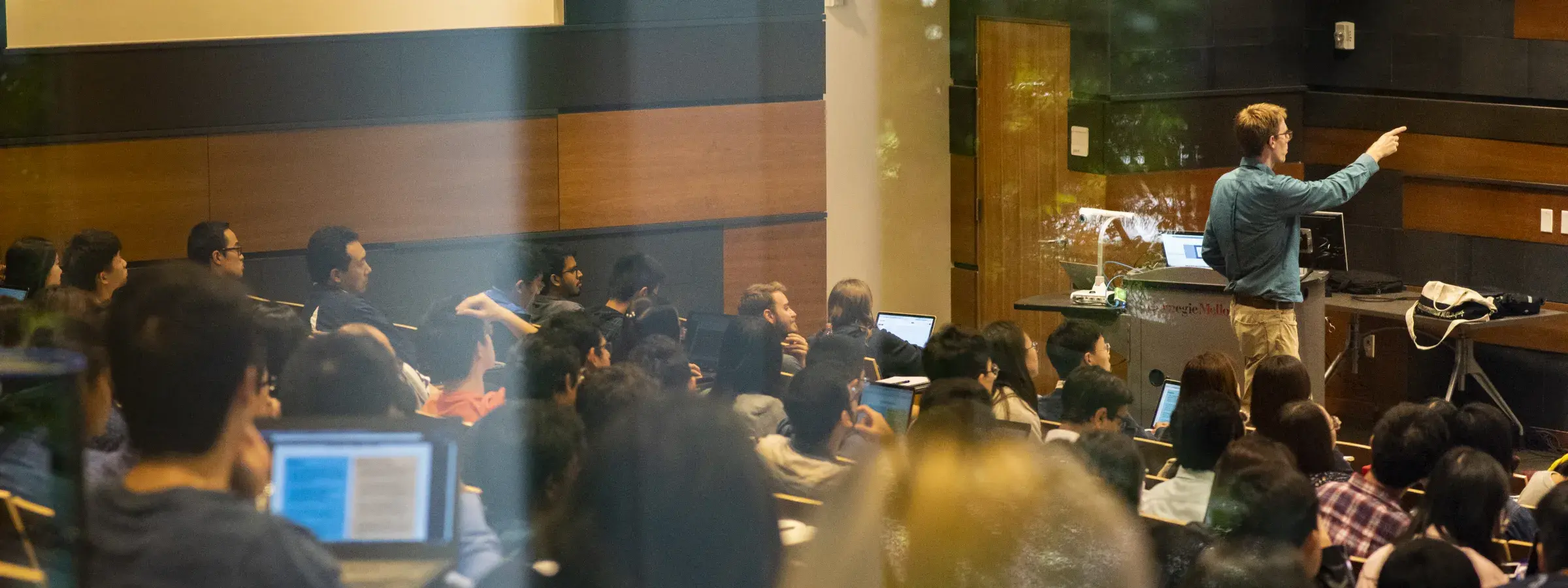 professor pointing toward front of classroom in room full of students