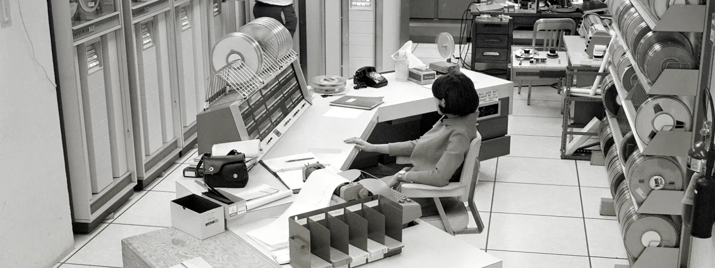 black and white image of two people in computer room with tape driven mainframe computers