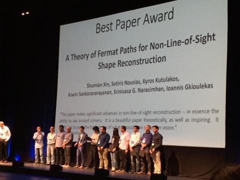 Research group faculty and students on stage in front of projected text awarding CVPR 2019 Best Paper Award